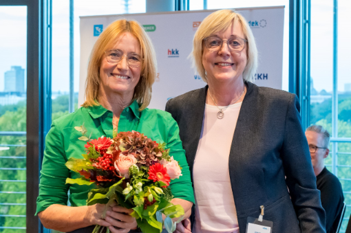 Eine Frau mit Blumenstrauß neben einer anderen Frau vor Banner mit Logos